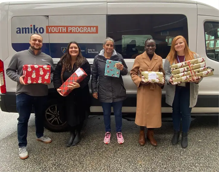 Group photo of people holding presents in front of a sprinter van that says amiko youth program
