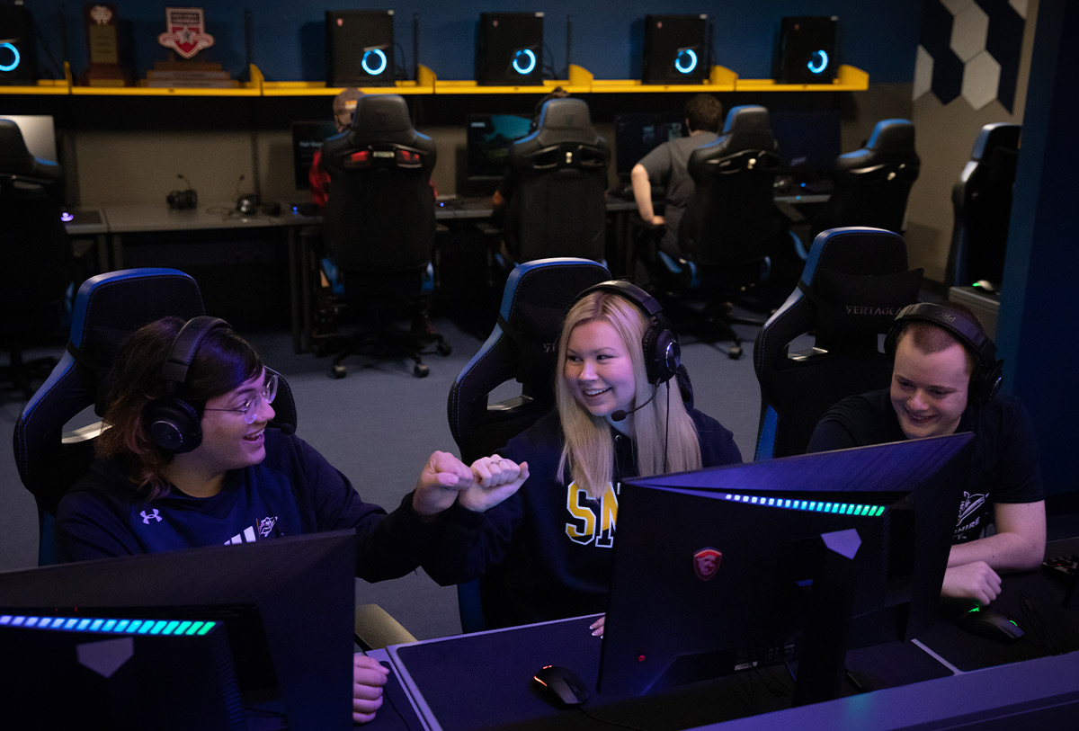 students smiling and fist bumping while sitting in front of computers at the SNHU esports complex