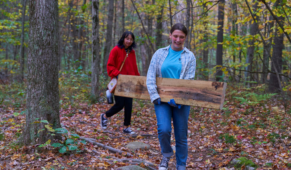two volunteers carrying a piece of wood through the woods