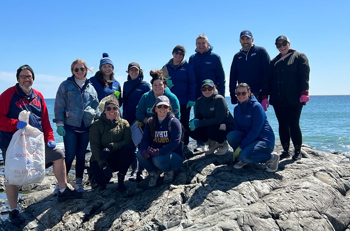 a group of SNHU Global Days of Service volunteers take a photo while on a rock with the ocean in the background