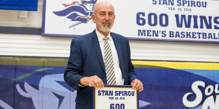 Stan Spirou holding 600 wins sign on basketball court inside of gym