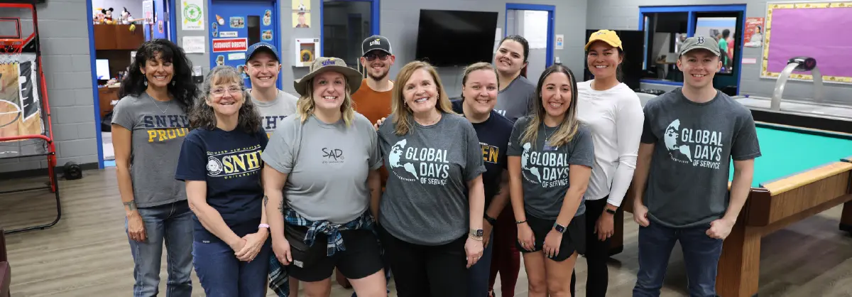 Landscape orientation close-up indoor photograph view of SNHU alumni and staff all smiling gathered together for a group photo at the Boys & Girls Clubs of Tucson