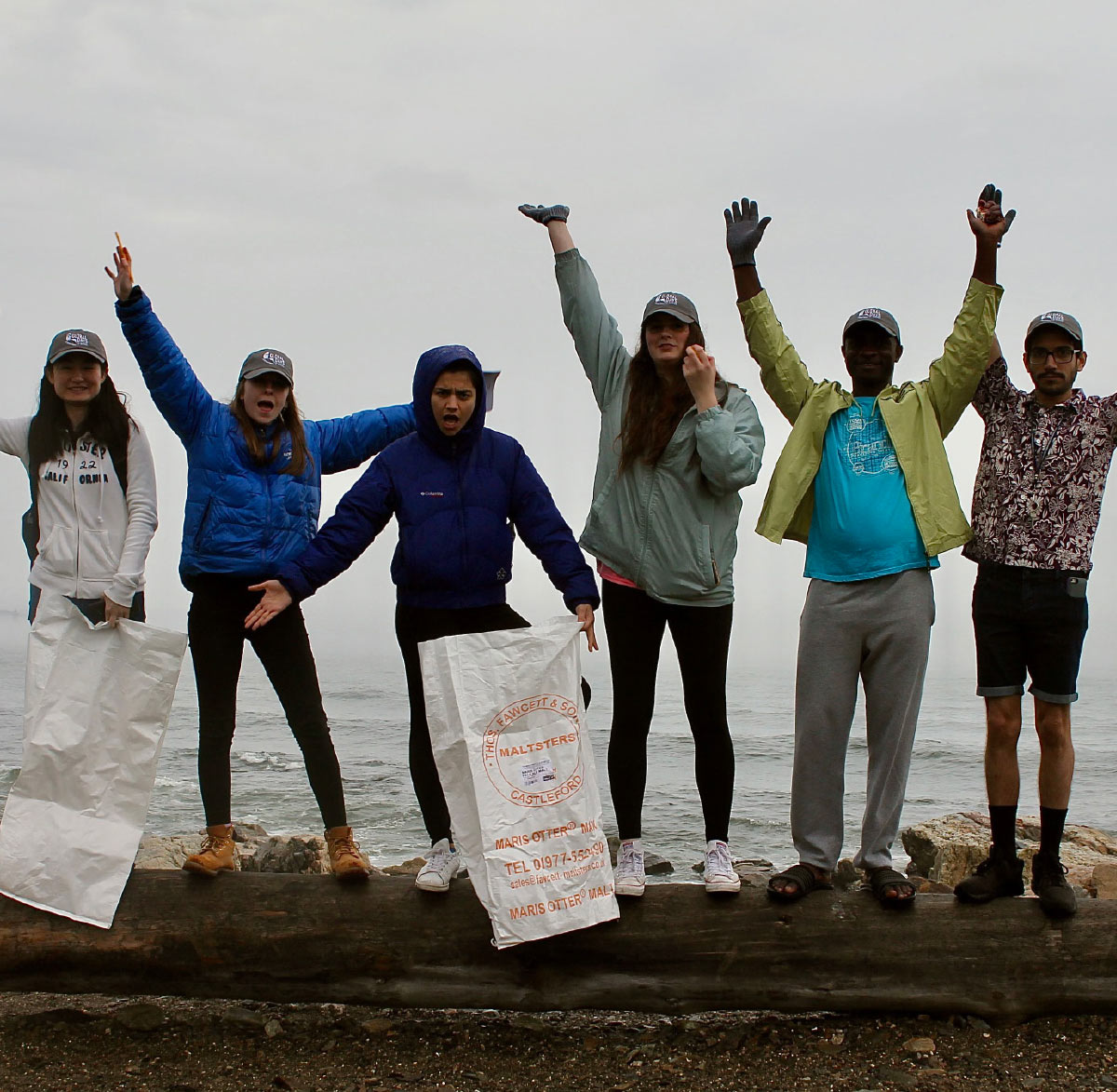 students in a line side by side standing on a log by ocean water