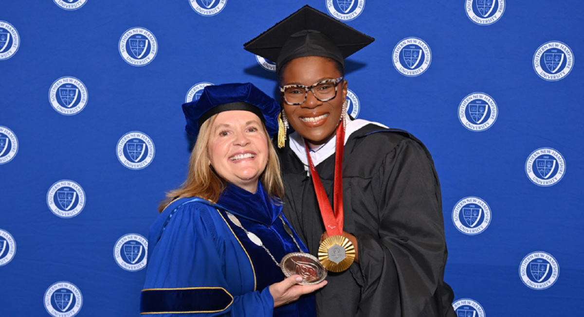 Lisa Marsh Ryerson with grad Nicky Nieves ’25G smiling for a photo while wearing medals and cap and gowns