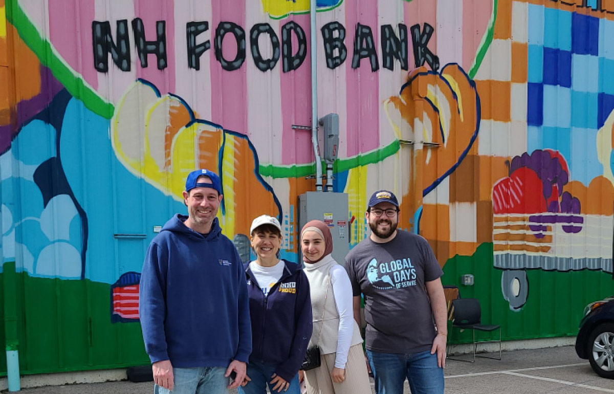 a group photo of four people standing outside of the NH Food bank