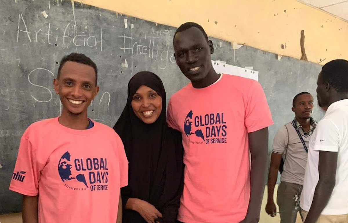 group photo of two men wearing matching pink Global Days of Service shirts and a woman in front of a chalkboard