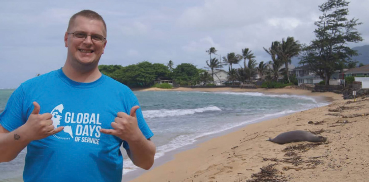 man wearing blue Global Days of Service shirt smiling at the beach