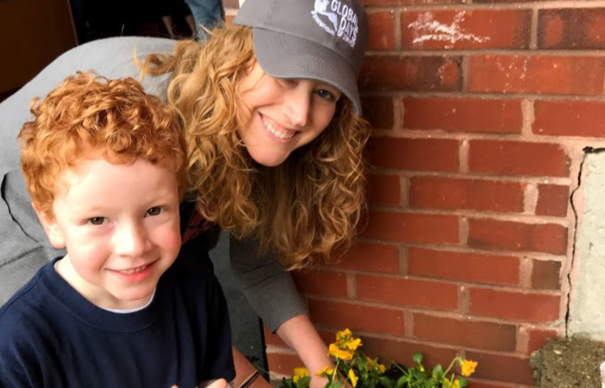 Sara Telfer and her son smiling while planting yellow flowers in front of a brick building
