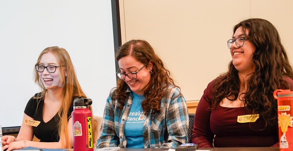 Three people sitting at a table, smiling, with water bottles in front of them.