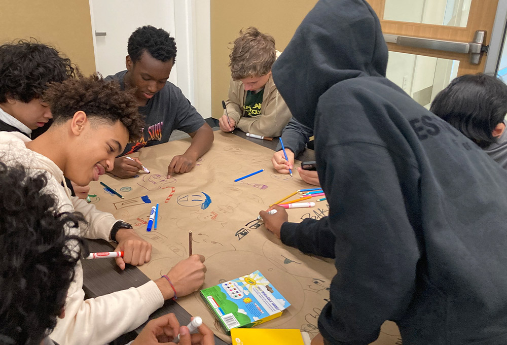 a group of young men sit around a table doodling on craft paper