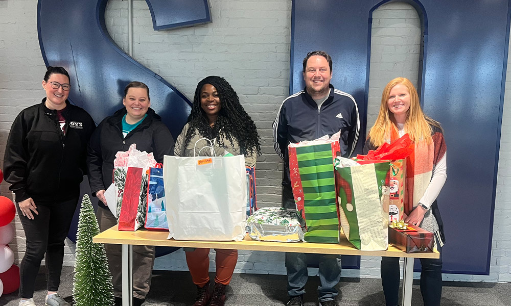 five adults smile while standing behind a table covered with gift bags