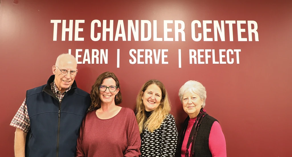 Four adults standing together in front of a red wall with the text “The Chandler Center – Learn | Serve | Reflect.”